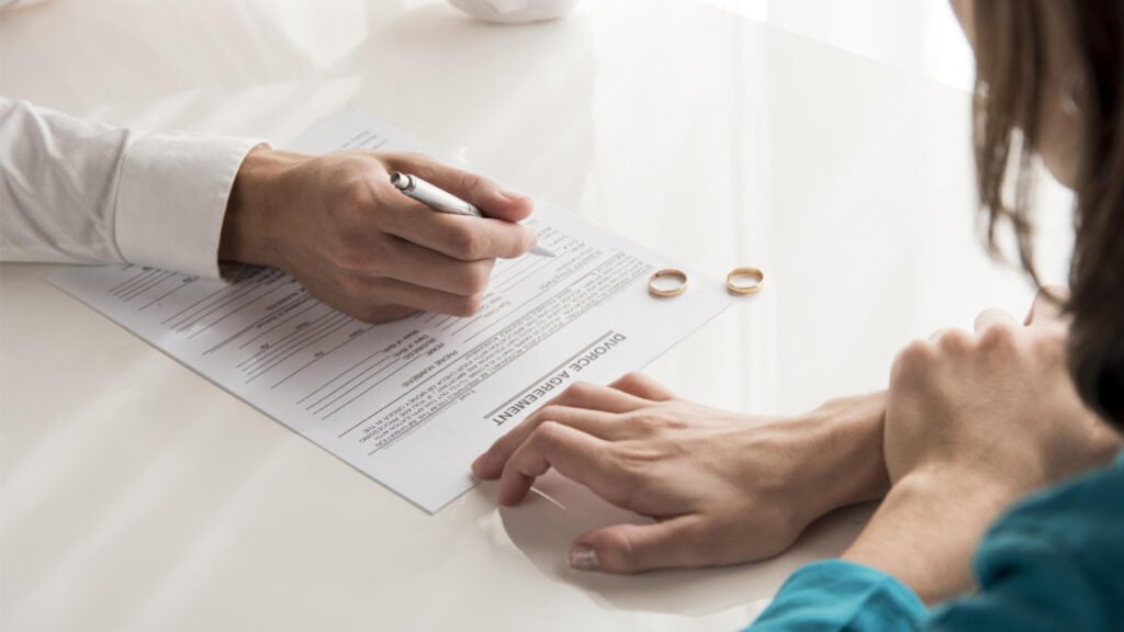 Mulher lendo um contrato de divórcio com duas alianças sobre a mesa
